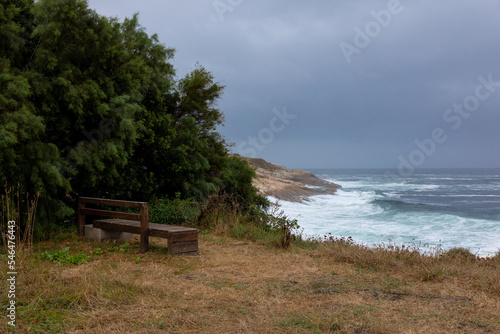 A bench with a beautiful view of the ocean with waves in cloudy weather and clouds.