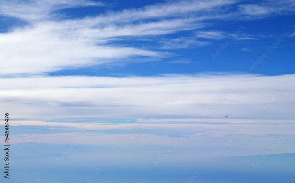 Vivid blue sky and white spreading clouds with an airplane flying in distance view during the flight