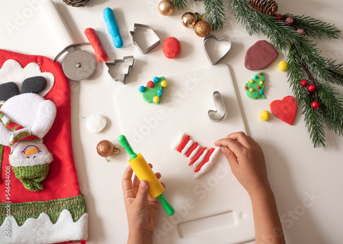 Child's hands playing with colorful dough on white background and do red-white strip for toy gift bag. Development game sculpting figures from dough. Tasty christmas cookies. top view