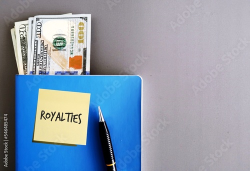 Cash money in dollars and a pen on a blue notebook, isolated on grey background, concept of legally payment made on using their intellectual property assets, including book copyrights  photo