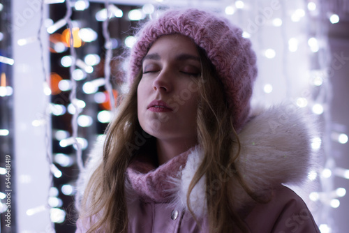 Bright color photo portrait of a beautiful girl in a pink hat with luminous garlands and beautiful bokeh outside in winter