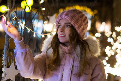 Bright color photo portrait of a beautiful girl in a pink hat with luminous garlands and beautiful bokeh outside in winter