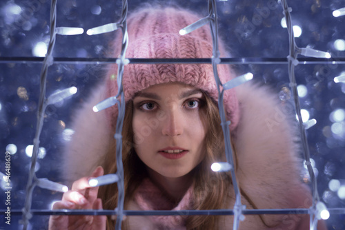 Bright color photo portrait of a beautiful girl in a pink hat with luminous garlands and beautiful bokeh outside in winter