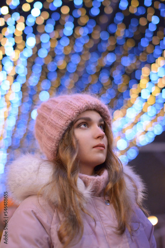 Bright color photo portrait of a beautiful girl in a pink hat with luminous garlands and beautiful bokeh outside in winter