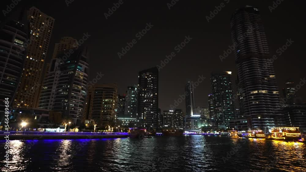 View of beautiful and developed city with skyscrapers at night. Buildings illuminated with neon color lights on seashore. Modern metropolis streets. Urban architecture. Reflection of lights in water. View of beautiful and developed city with skyscrapers at night. Buildings illuminated with neon color lights on seashore. Modern metropolis streets. Urban architecture. Reflection of lights in water.