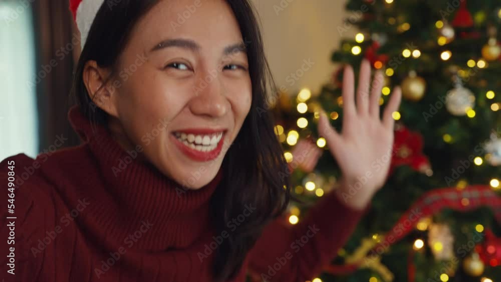 Close-up Young Asia beauty female blogger looking at camera video call say merry christmas and happy new year, Christmas tree decorated with ornament in living room at home. Holiday festival concept. Close-up Young Asia beauty female blogger looking at camera video call say merry christmas and happy new year, Christmas tree decorated with ornament in living room at home. Holiday festival concept.