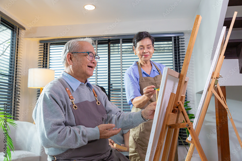 Couple Senior drawing at art. Side view portrait of white haired senior woman holding palette painting pictures at easel in art studio. Couple Senior drawing at art. Side view portrait of white haired senior woman holding palette painting pictures at easel in art studio.