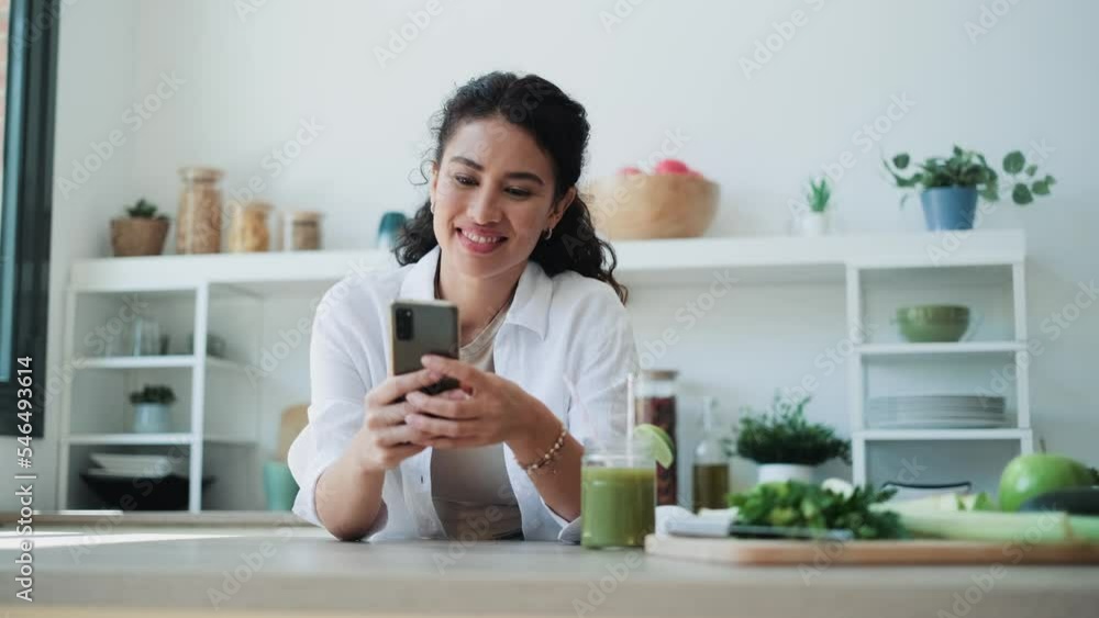 Video of pretty woman using her mobile phone while drinking fruit detox juice in the kitchen at home. Video of pretty woman using her mobile phone while drinking fruit detox juice in the kitchen at home.