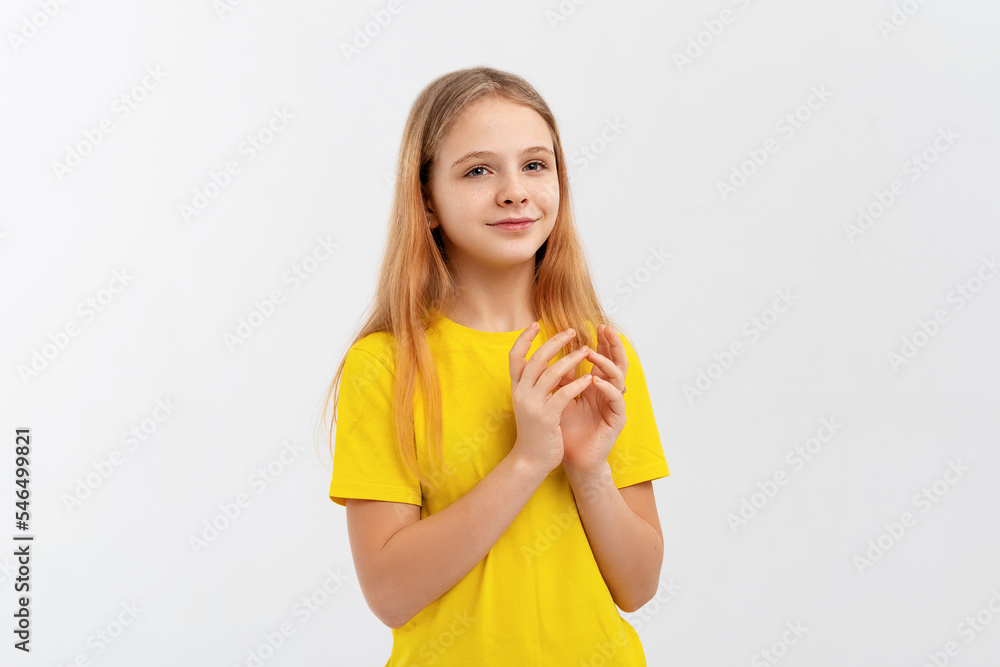 Lovely teen girl in yellow t-shirt, rubs hands and smiles, relish smth good, applause, looks happy, stands over white background Lovely teen girl in yellow t-shirt, rubs hands and smiles, relish smth good, applause, looks happy, stands over white background