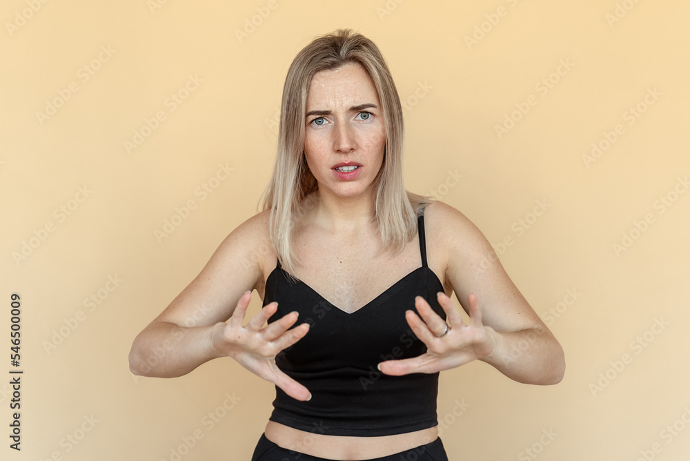 Portrait of the scared young woman with freckles shows stop gesture with hands. Worried girl wearing casual black clothes standing over beige background. Panic concept Portrait of the scared young woman with freckles shows stop gesture with hands. Worried girl wearing casual black clothes standing over beige background. Panic concept