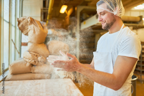 Junger Mann als Bäcker Lehrling klatscht Mehl von den Händen photo