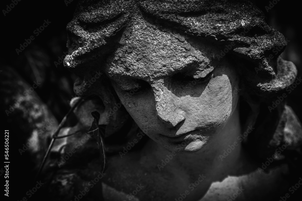 Black and white image og sad angel as symbol of pain, fear and end of life. Close up fragment of an ancient stone statue.