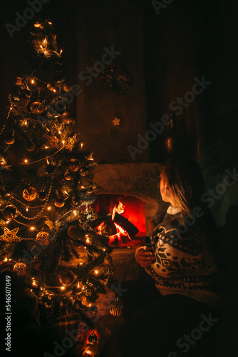 Woman Decorating the Christmas tree with golden decorations on it next to the fireplace. Christmas Eve concept. 