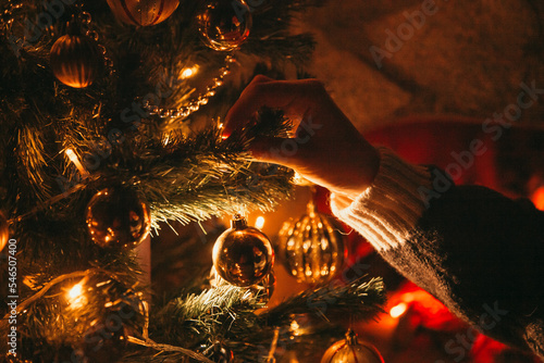 Decorating the Christmas tree with golden decorations on it next to the fireplace. Christmas Eve concept. 