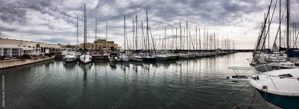 Panoramic view at marina with many sail boats and pleasure boats moor in the safe port basin in a bad weather day with dramatic sky