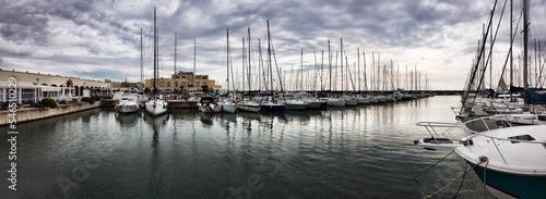 Panoramic view at marina with many sail boats and pleasure boats moor in the safe port basin in a bad weather day with dramatic sky photo