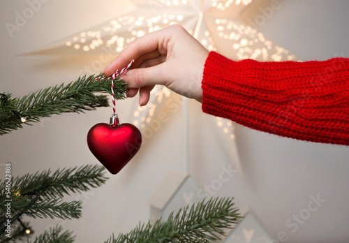 closeup of Female hands holding Christmas ornament heart shape for decorating fir tree. Winter holidays banner