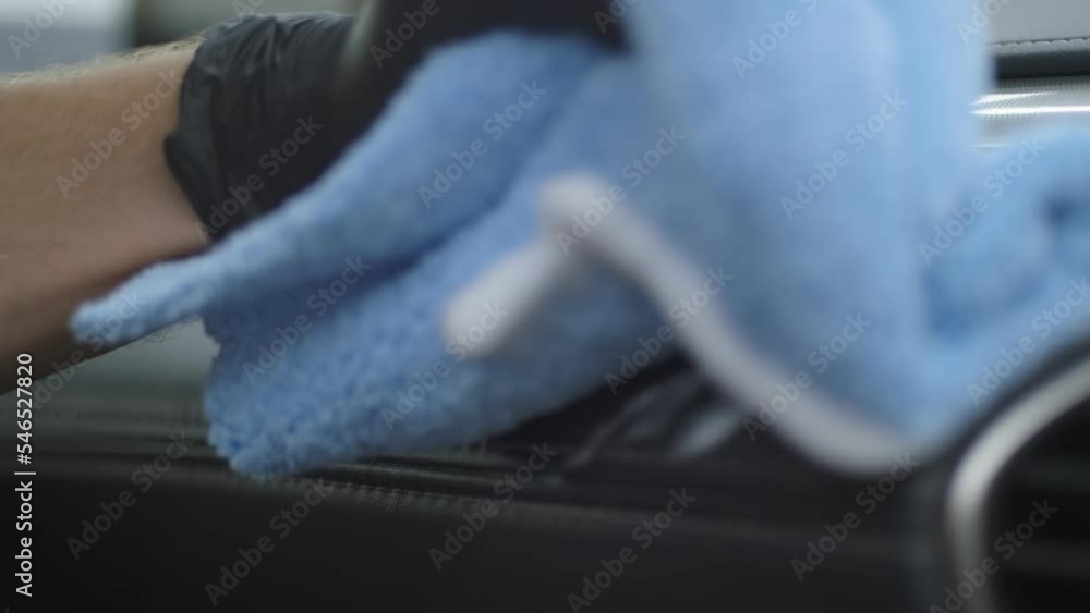 Close up of a Hand in black glove Washing car interior dashboard by blue microfiber cloth with the detergent. Serviceman does dry cleaning in the car Close up of a Hand in black glove Washing car interior dashboard by blue microfiber cloth with the detergent. Serviceman does dry cleaning in the car