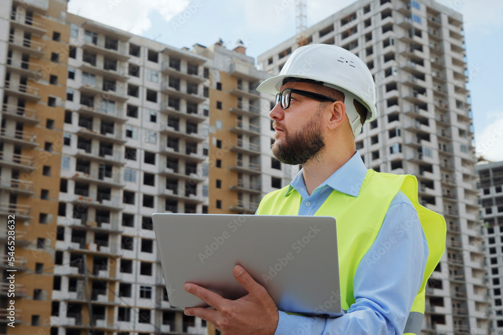 Bearded building inspector working on laptop at construction site