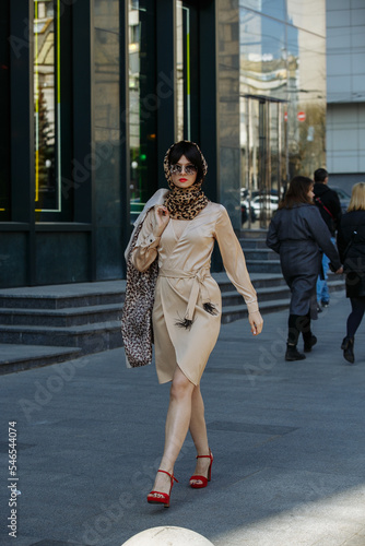 A gorgeous girl in a dress and glasses walks around the city on a sunny day