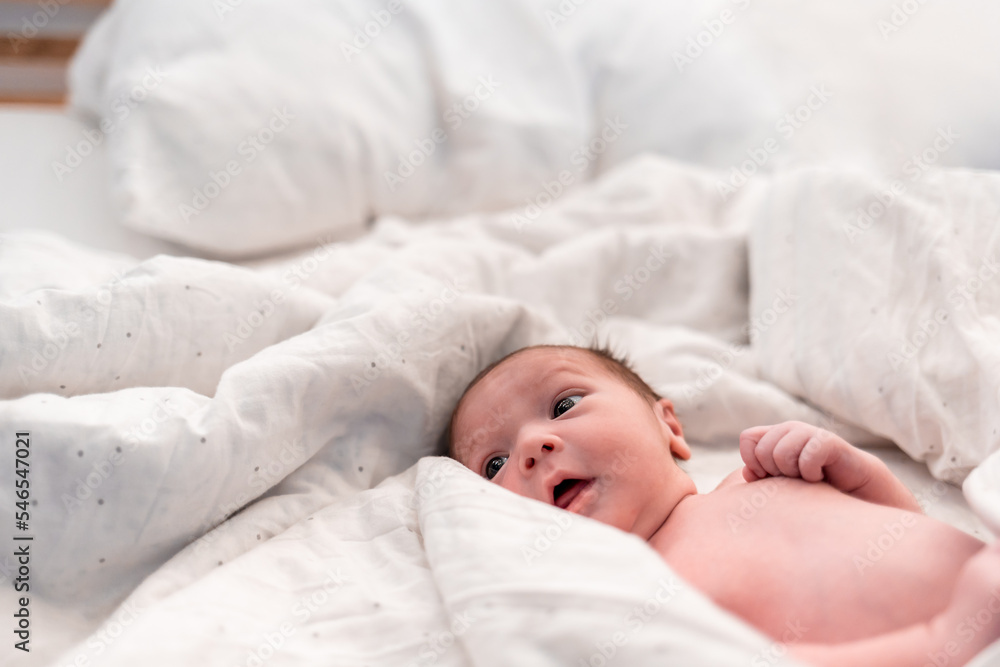 Calm newborn baby child lying in white bed sheets Calm newborn baby child lying in white bed sheets