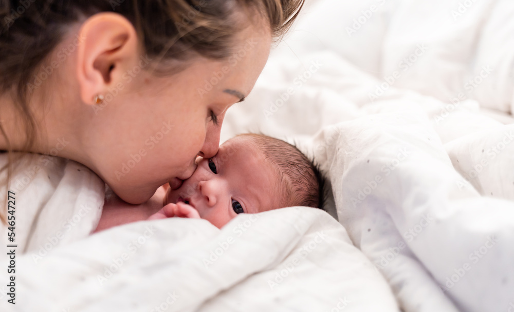 Loving mom kissing her newborn baby child lying in bed Loving mom kissing her newborn baby child lying in bed