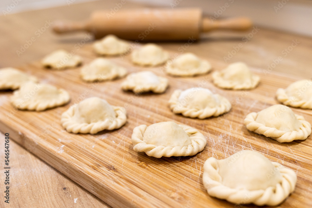 Raw dumplings polish traditional perogies lying on wooden board in kitchen