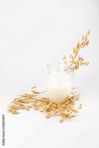 Oat milk in a jug and oat spike on light background. Vegan non dairy alternative milk.
