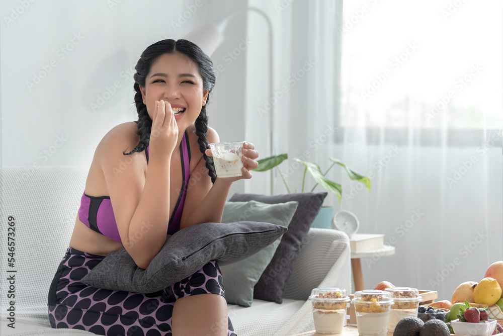 happy beautiful young woman sit on sofa having healthy breakfast at home with fruit and nature yogurt, wellbeing diet concept.