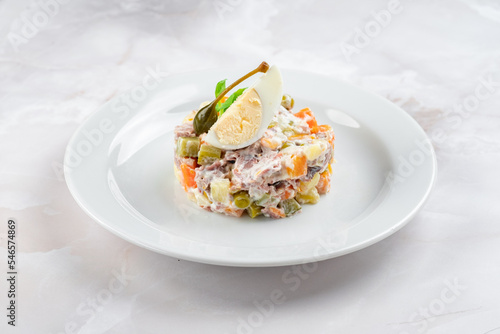 Russian salad olivier decorated dish on a white plate. Hearty salad of potatoes, carrots, peas, egg, cucumbers and mayonnaise