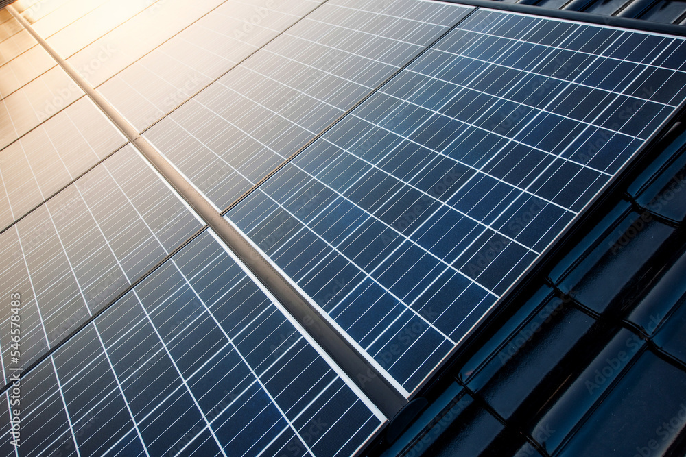 New solar panels are mounted on a roof with shiny black tiles and the clear sky is reflected in the warm sunlight in it. New solar panels are mounted on a roof with shiny black tiles and the clear sky is reflected in the warm sunlight in it.