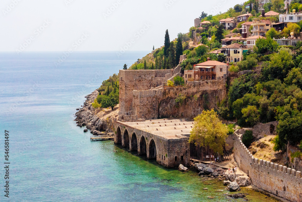 Fototapeta premium Ancient shipyard (Tersane) near of Kizil Kule tower in Alanya, Turkey (Turkiye) Famous tourist destination with high mountains. Beautiful beach and calm turquoise sea surface. copy space