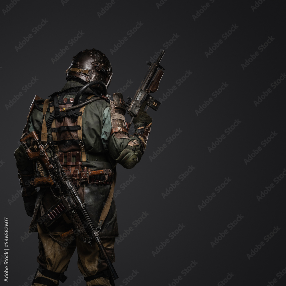 Back view shot of post apocalyptic stalker holding shotgun against grey background. Back view shot of post apocalyptic stalker holding shotgun against grey background.