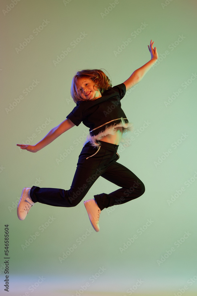 Dance, fun, joy. Happy little girl, kid in casual clothes jumping high isolated over light background. Kids fashion, emotions, carefree childhood