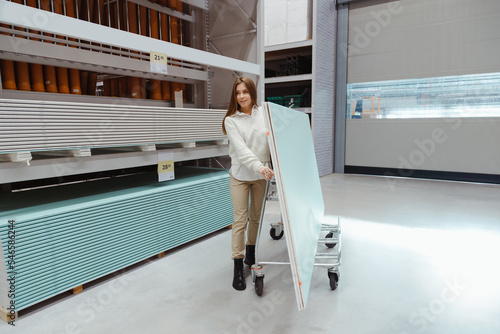 Young woman carrying trolley cart with drywall sheets in hardware store photo