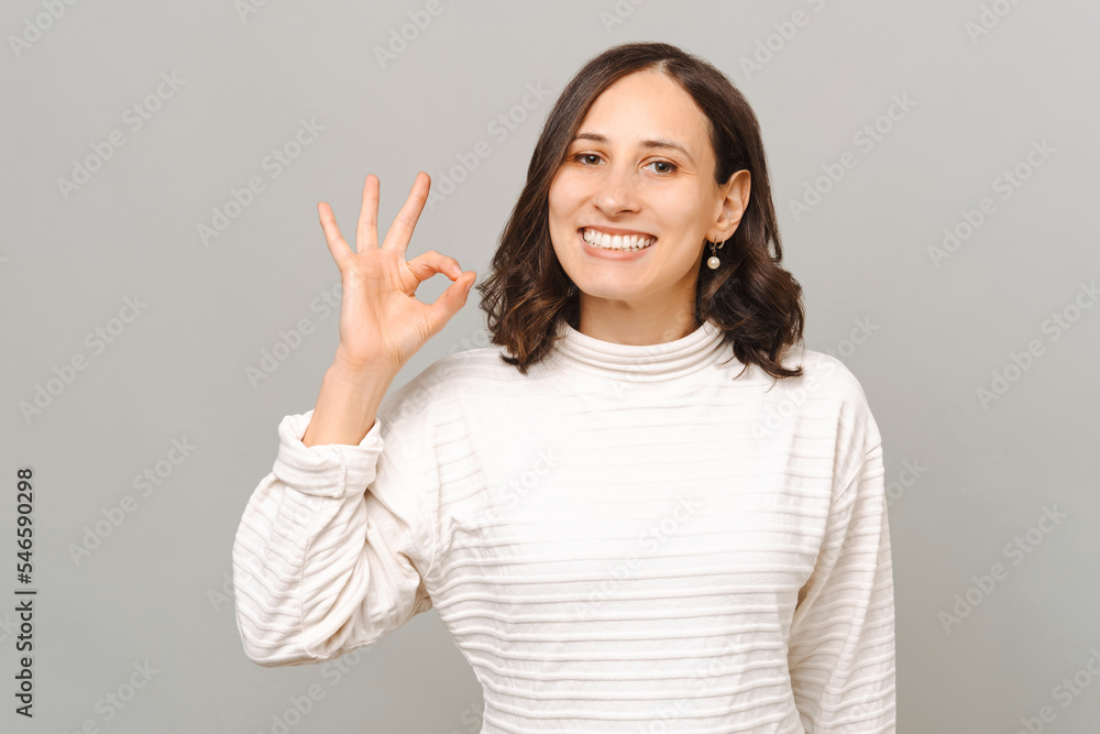 Pleased young woman shows ok gesture while smiling at the camera in a studio. Pleased young woman shows ok gesture while smiling at the camera in a studio.