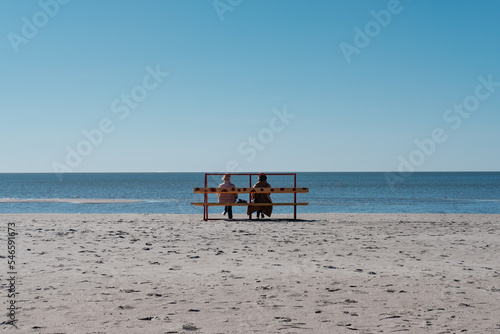Dwie kobiety siedzą na ławce na piaszczystej plaży w słoneczny dzień