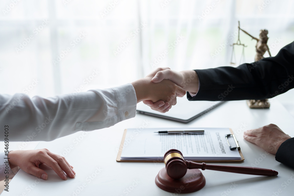 Lawyer shaking hands with a client making about documents, contracts, agreements, cooperation agreements with a female client at the lawyer's desk and a hammer at the table. - obrazy, fototapety, plakaty 
