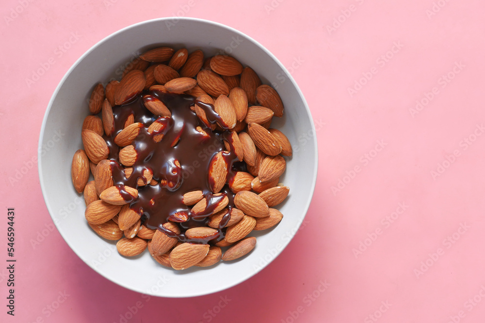 dark chocolate cream pouring on almond nuts in a bowl on pink dark chocolate cream pouring on almond nuts in a bowl on pink