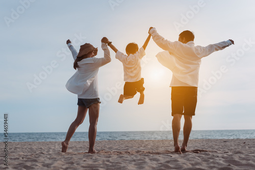 Happy asian family jumping together on the beach in holiday vacation. Silhouette of the family holding hands enjoying the sunset on the sea beach. Happy family travel, trip family holidays weekend.