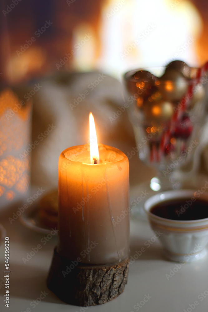 Glass with Christmas ornaments, cup of tea, cookies, candles and knitted blanket by the fireplace. Cozy Christmas at home. Glass with Christmas ornaments, cup of tea, cookies, candles and knitted blanket by the fireplace. Cozy Christmas at home.