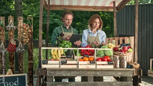 Wallpaper Mural Happy mature male and female farmers standing at stall selling farm vegetables and fruits and talking. Caucasian family couple using gadget typing on tablet device working at food market outdoor. Torontodigital.ca