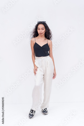 A slim and pretty Filipino woman with long curly hair in her early 20s. Wearing a black spaghetti strap blouse and white pants. Isolated on a white background. © Mdv Edwards