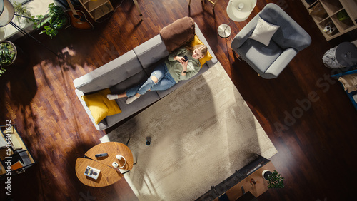 Foto Apartment: Young Woman Uses Smartphone Lying on Her Couch in Living Room