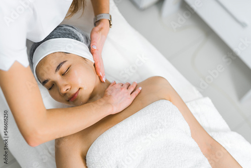 Young beautiful Asian woman receiving a professional neck massage at an aesthetic salon. Unrecognizable Caucasian beautician doing relaxing massage on her female client. High quality photo