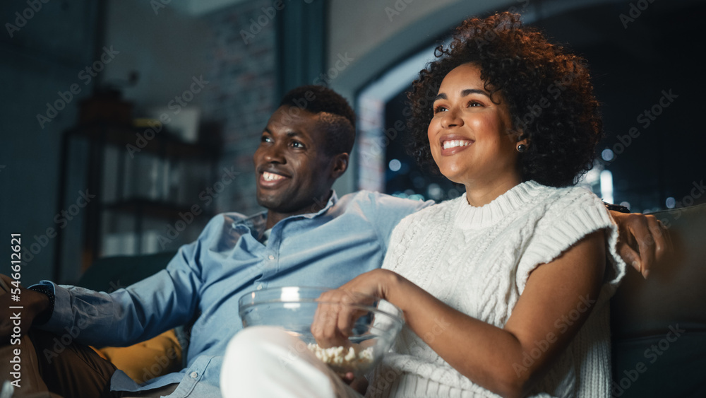 Foto de Black Couple Watching Comedy Movie on TV, Eating Popcorn while Sitting on Couch in the