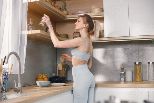 Fit woman in grey sportive costume standing on a kitchen