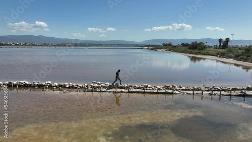 Uomo moro cammina lungo un lembo di terra che divide due stagni photo