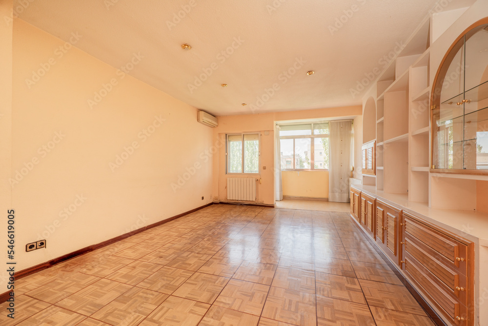 Fototapeta premium Empty living room with brick and plaster furniture and venetian style pinewood doors and a closed terrace in the background with aluminum windows