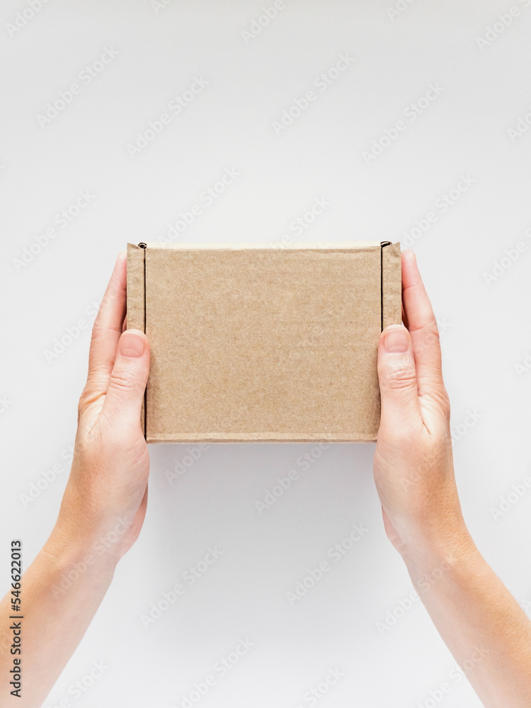 female hands holding a small cardboard box on a white background. packaging and delivery concept, top view female hands holding a small cardboard box on a white background. packaging and delivery concept, top view